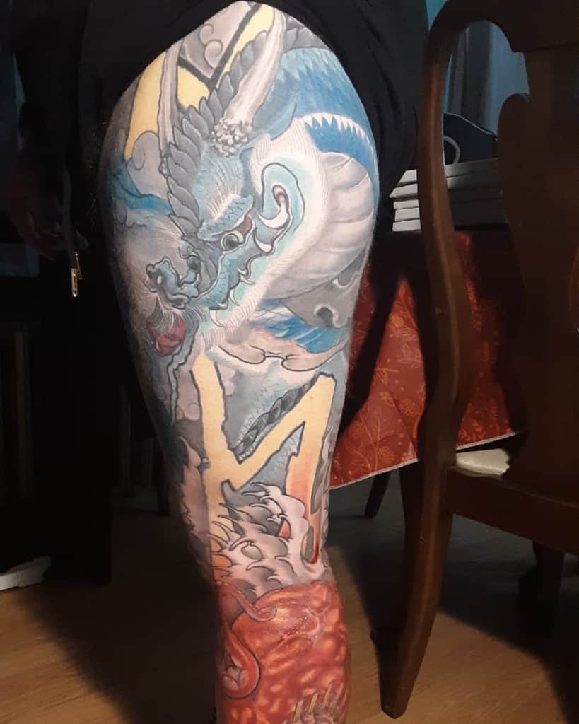 A colorful leg sleeve blue and white dragon tattoo featuring yellow background, waves, tentacle and red thing below