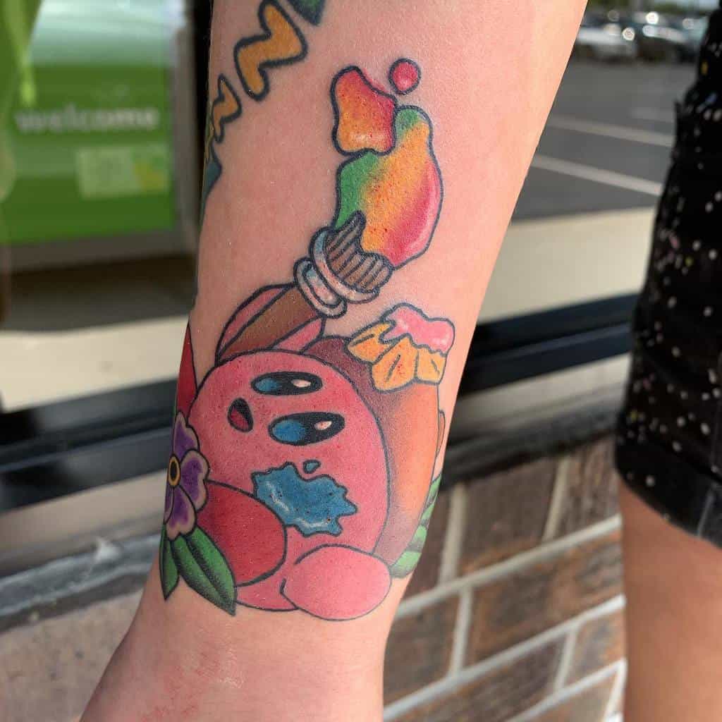 Kirby tattoo with a paintbrush, colorful paint, and floral details, a vibrant and artistic design capturing Kirby’s painter ability