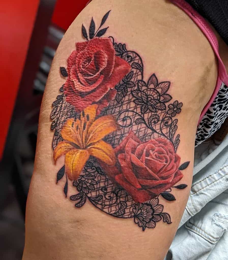 Vibrant tattoo featuring red roses, an orange lily, and intricate black lace details, blending bold realism with delicate ornamentation