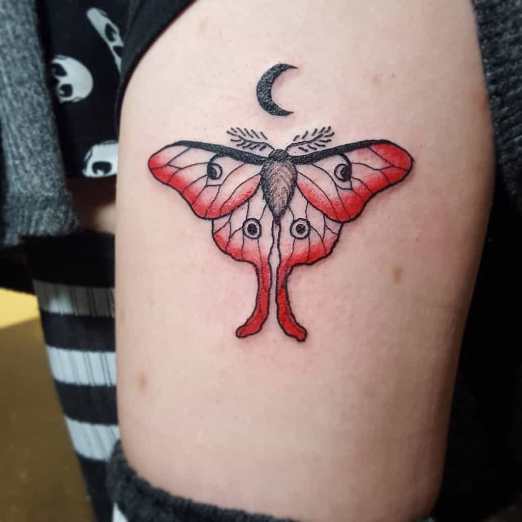 A tattoo of a Luna Moth with red and black wings, featuring eye details and a crescent moon above it