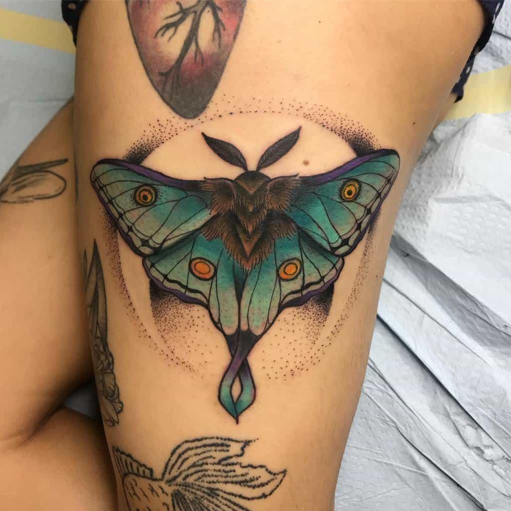 A vibrant Luna Moth tattoo, featuring teal wings, orange eyes, and detailed shading with a circular dot background
