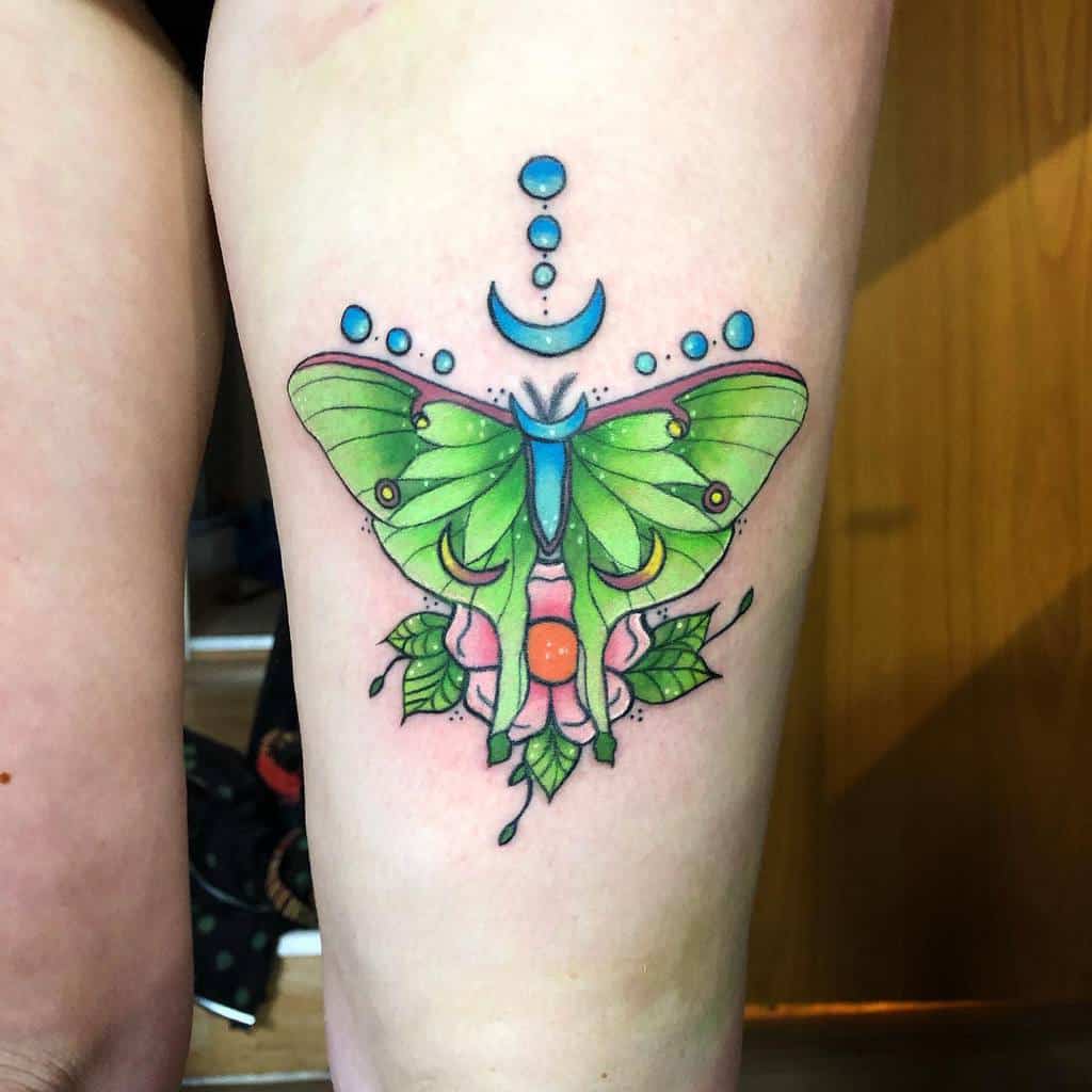 A colorful Luna Moth tattoo with green wings, a crescent moon, circular details, and floral accents beneath it