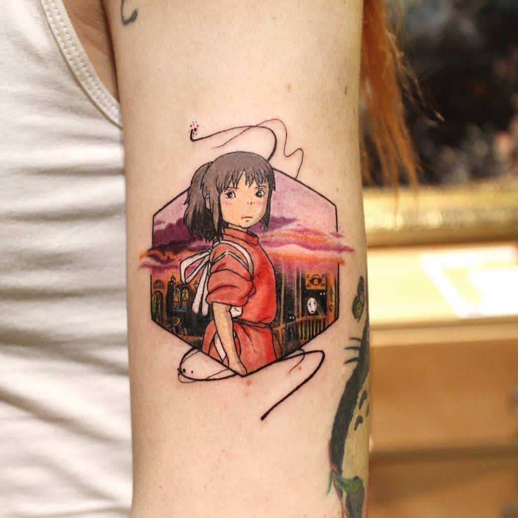 Beautiful Spirited Away tattoo of Chihiro standing before a sunset-lit bathhouse, framed in a hexagon with flowing artistic linework