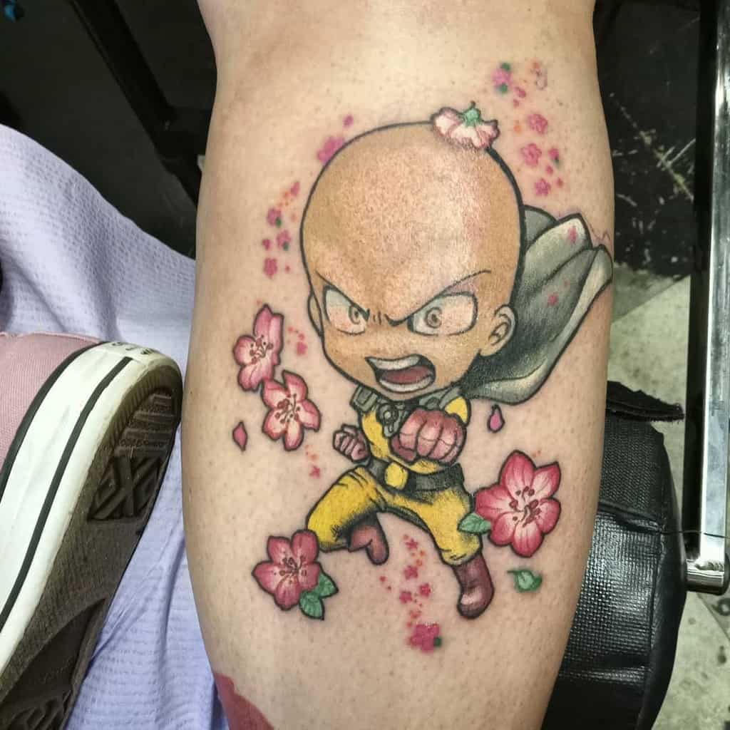 A chibi-style tattoo of Saitama from One Punch Man in a battle pose, surrounded by pink cherry blossoms with a flower on his head