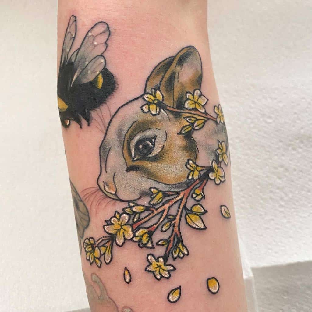 Tattoo of a rabbit surrounded by small yellow flowers on a branch and a bee