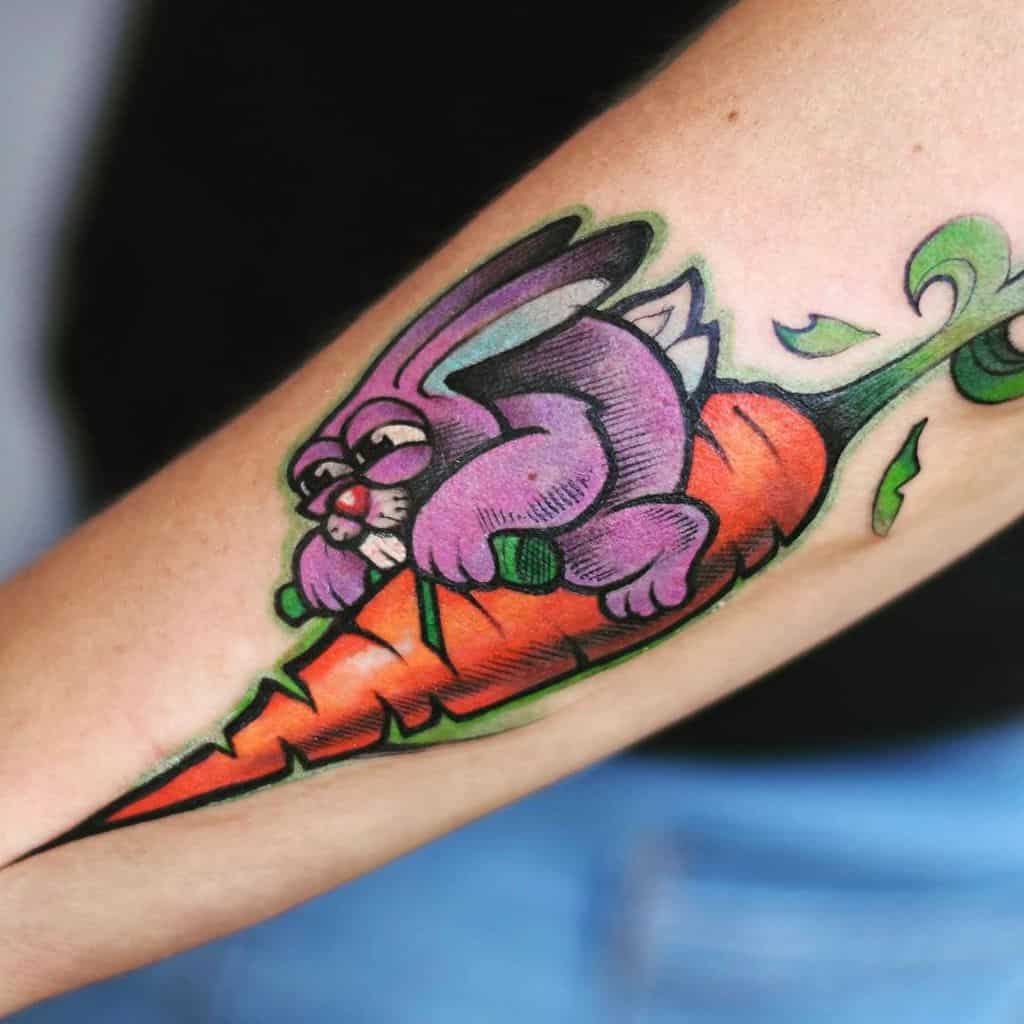 Bright and colorful tattoo of a purple rabbit sitting on a large carrot, with vibrant green leaves extending from the top