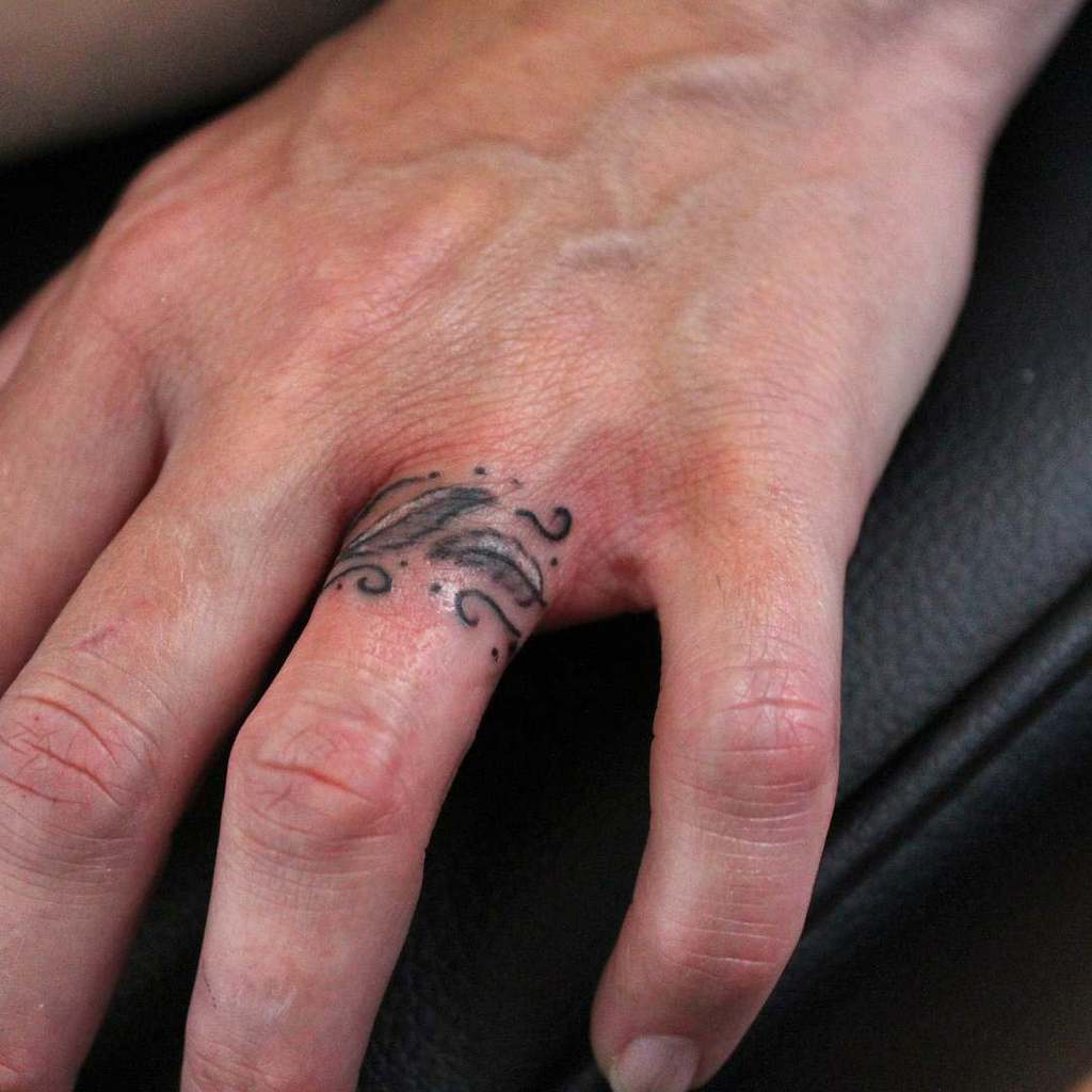 A delicate and artistic black ring tattoo with two feathers, with flowing swirls and soft shading