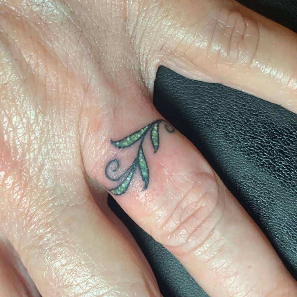 A delicate ring tattoo featuring green leaves with swirling black accents