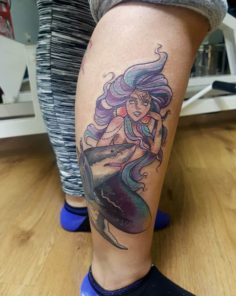 A colorful tattoo of a siren with flowing hair and a shark on a calf