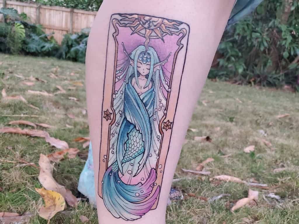 Enchanting tarot-style tattoo of a mermaid with flowing blue hair and tail, framed with celestial and ornate details