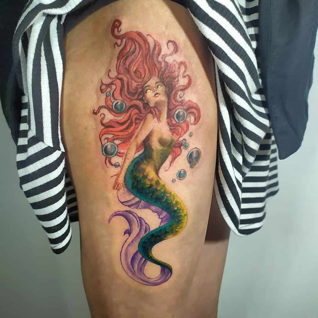Colorful thigh tattoo of a mermaid with flowing red hair, vibrant green and purple tail, surrounded by bubbles