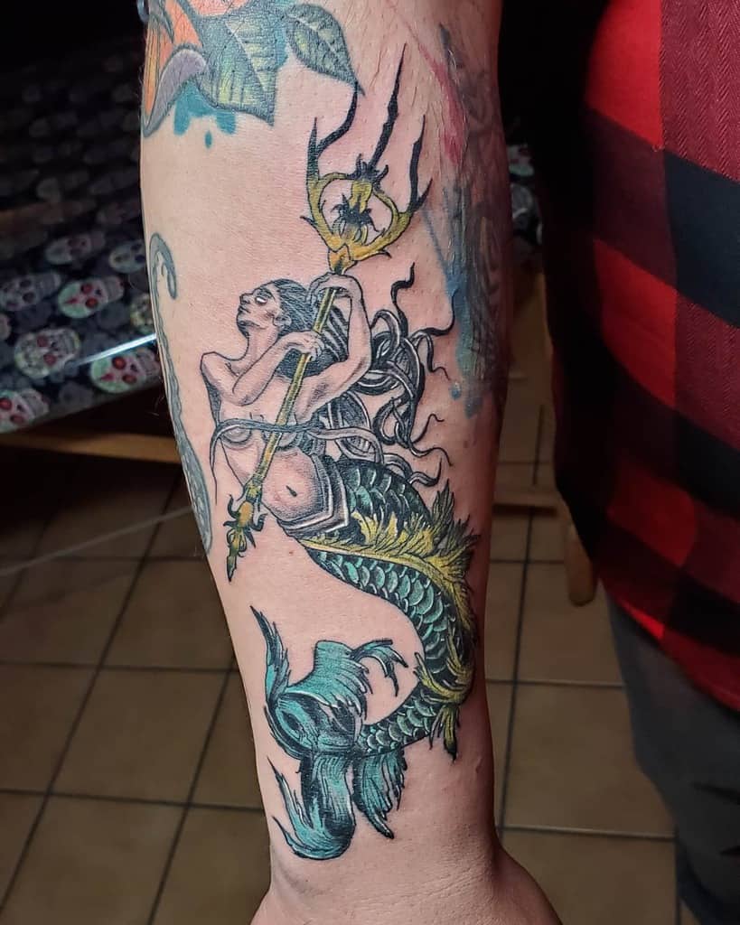Color tattoo of a fierce mermaid with a green and yellow tail, wild hair, holding a golden trident, designed in a fantasy style.