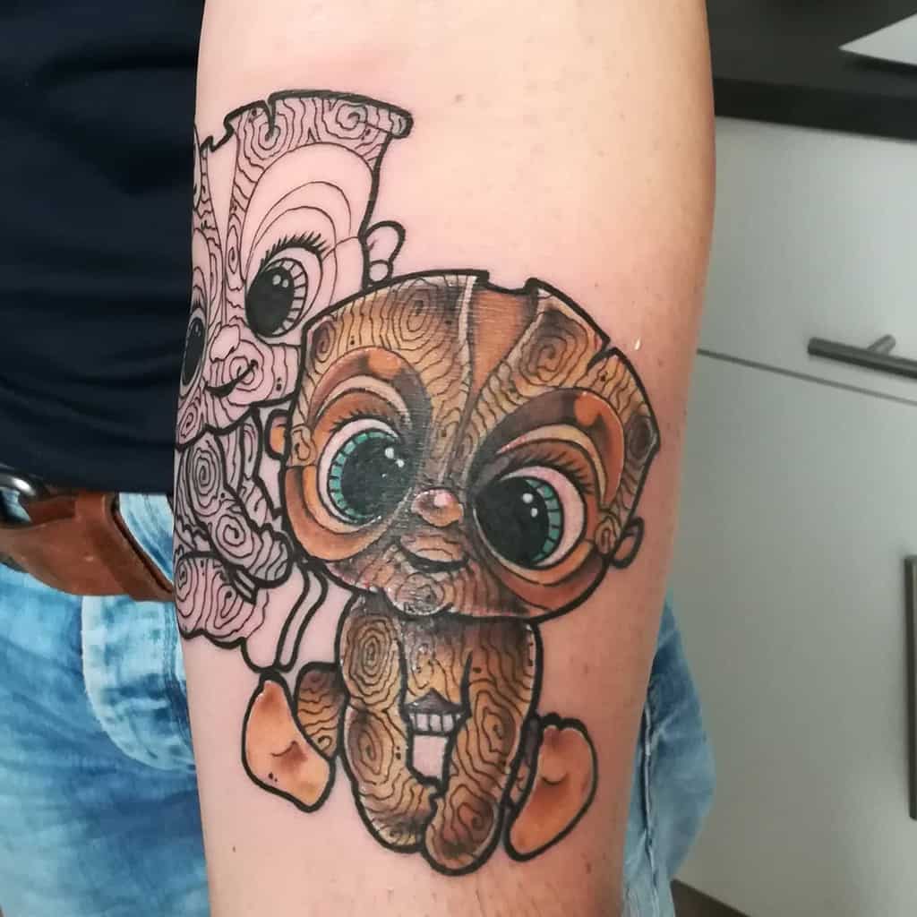 Playful Tiki tattoo featuring two cartoonish, wooden-style Tiki babies with large eyes, one colored in vibrant tones and the other outlined