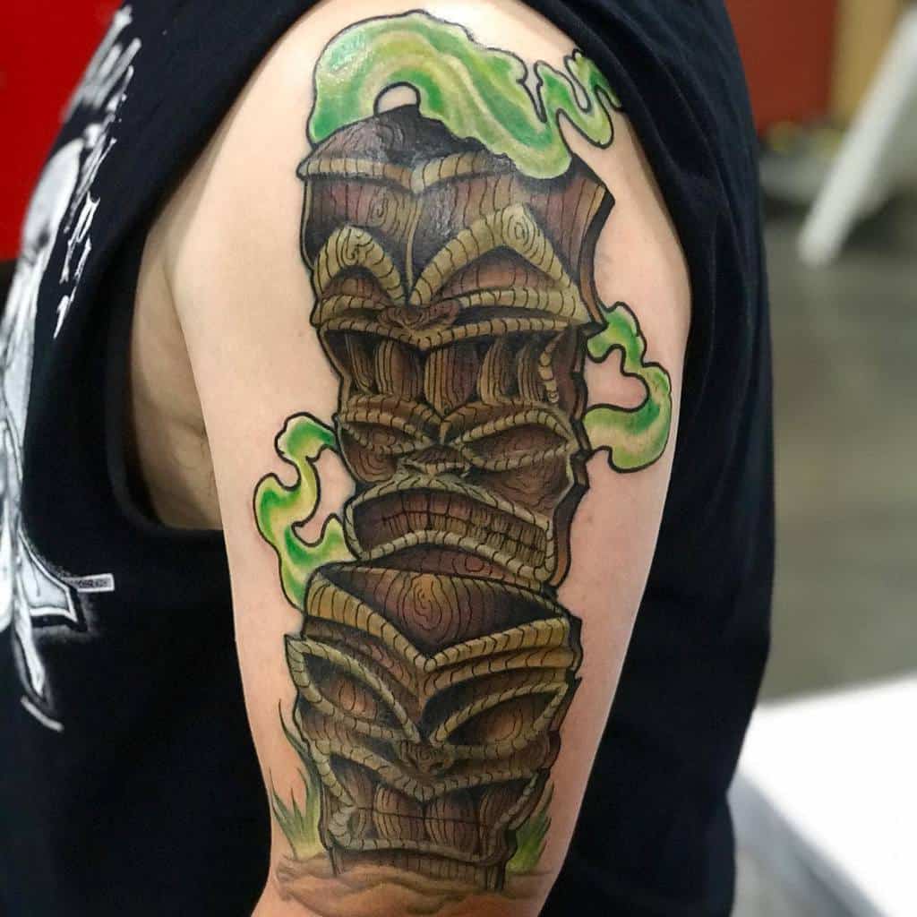 Colorful Tiki tattoo featuring a stack of three Tiki masks with intricate wooden details, surrounded by swirling green smoke