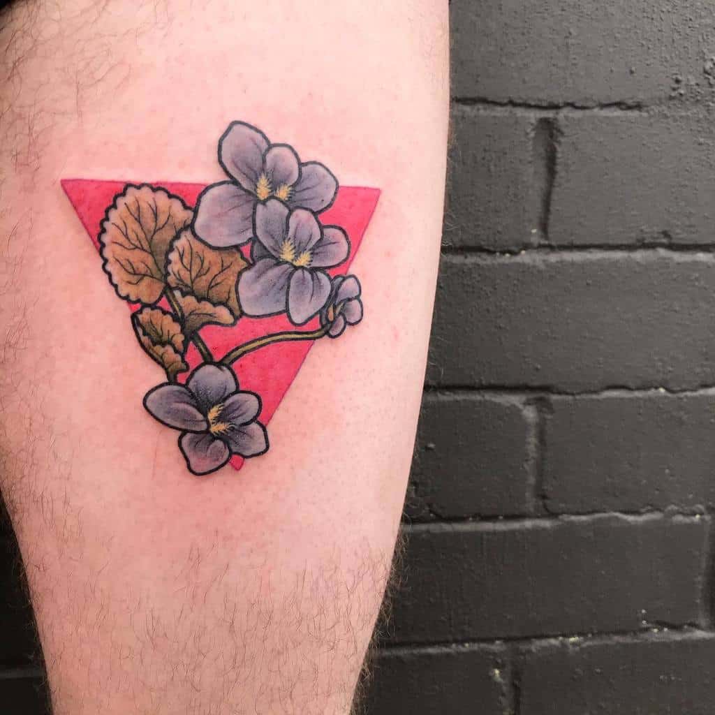 Bold tattoo of violet flowers with golden leaves over a vibrant red triangle, blending natural beauty with geometric contrast