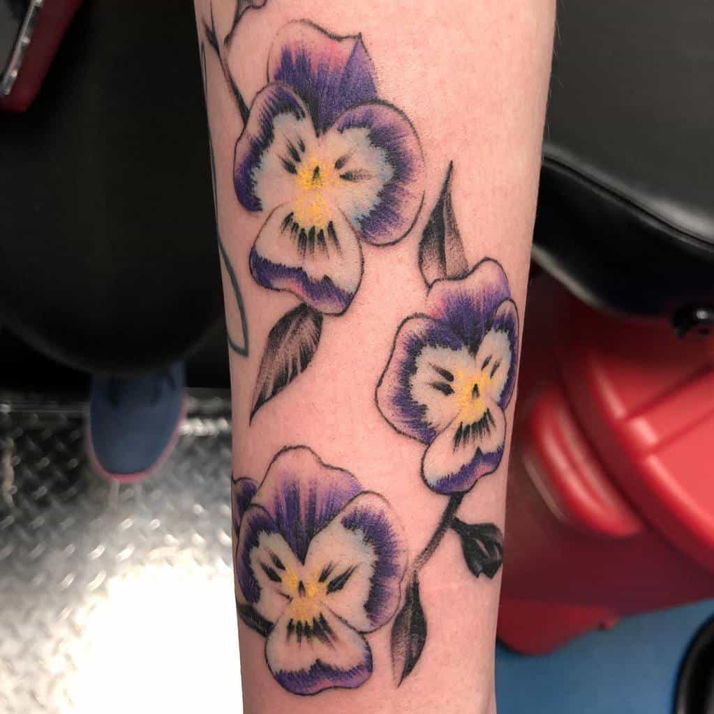 Vibrant tattoo of three violet pansy flowers with yellow centers, symbolizing love, remembrance, and admiration