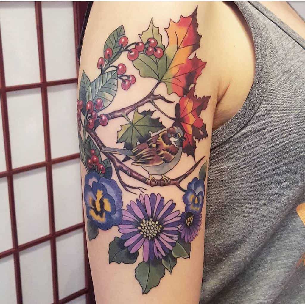 Colorful tattoo of a bird on a branch surrounded by autumn leaves, red berries, and violet flowers