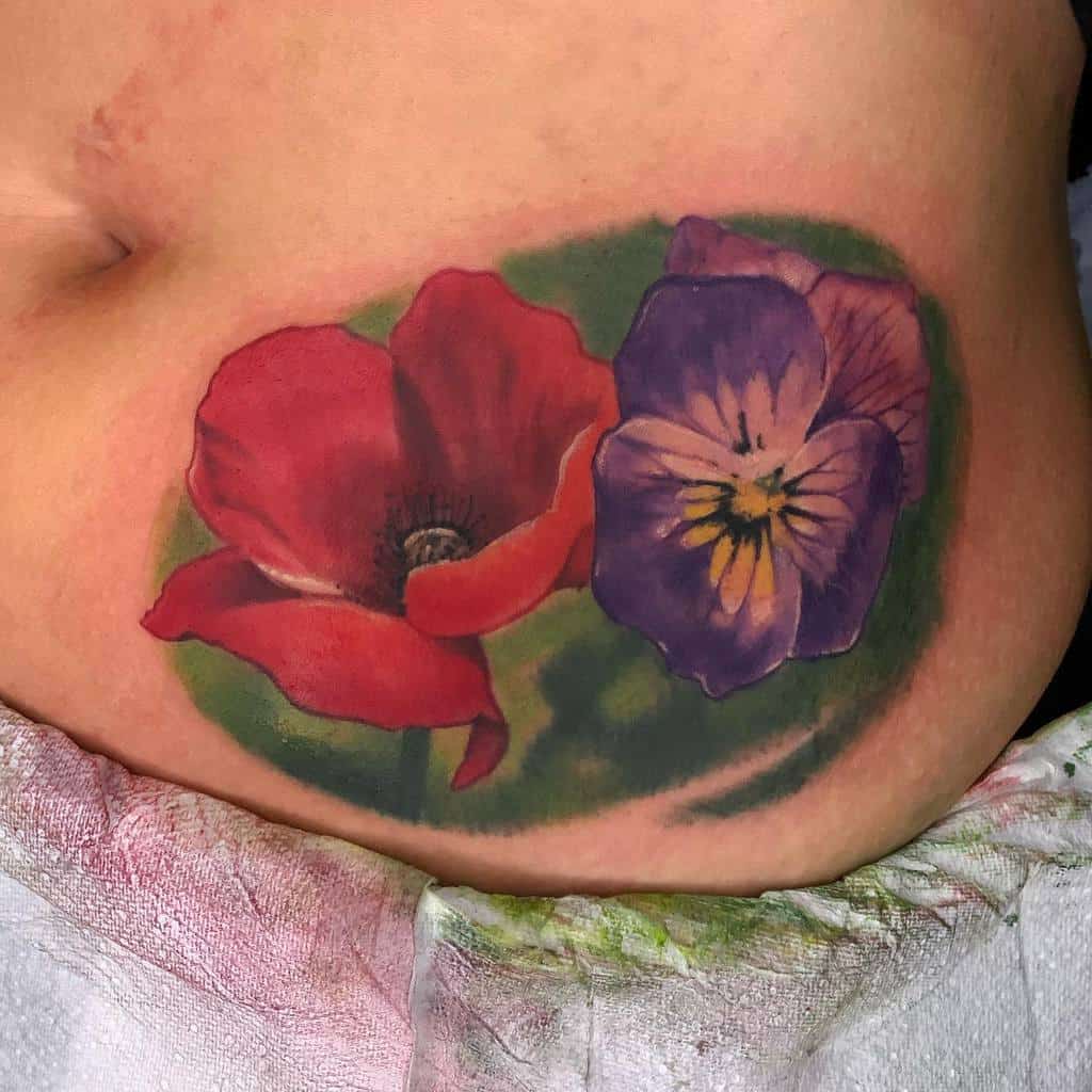 Realistic floral tattoo featuring a vibrant red poppy and a detailed purple pansy with a green background, symbolizing remembrance and love