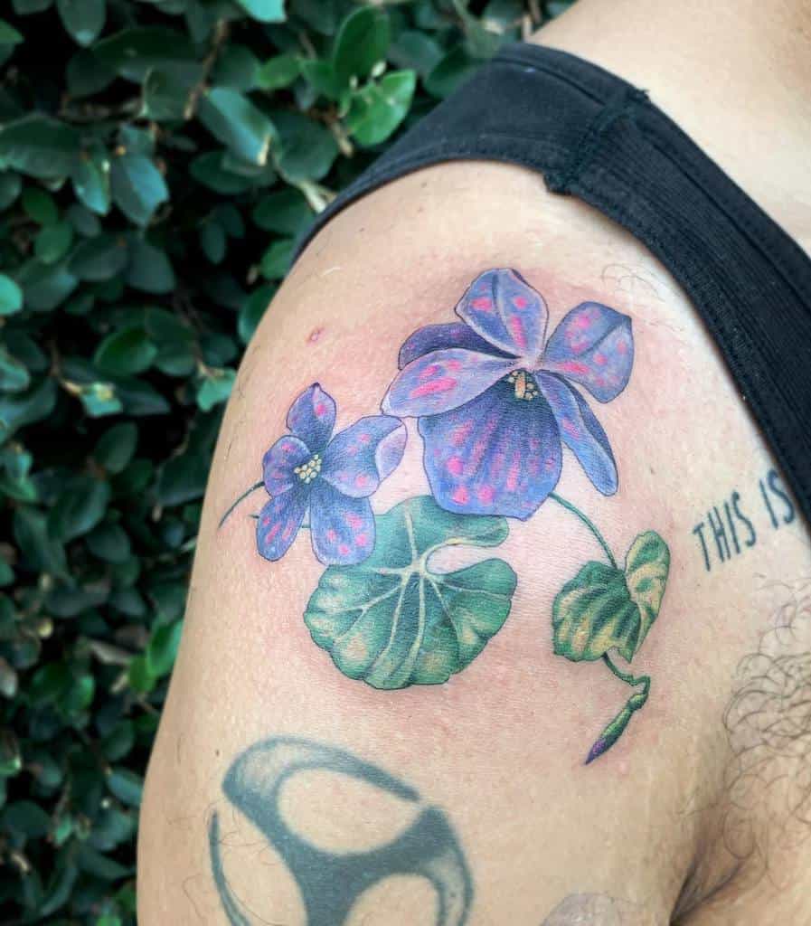 Realistic tattoo of vibrant two violet flowers with intricate shading and lush green leaves, symbolizing love, modesty, and remembrance