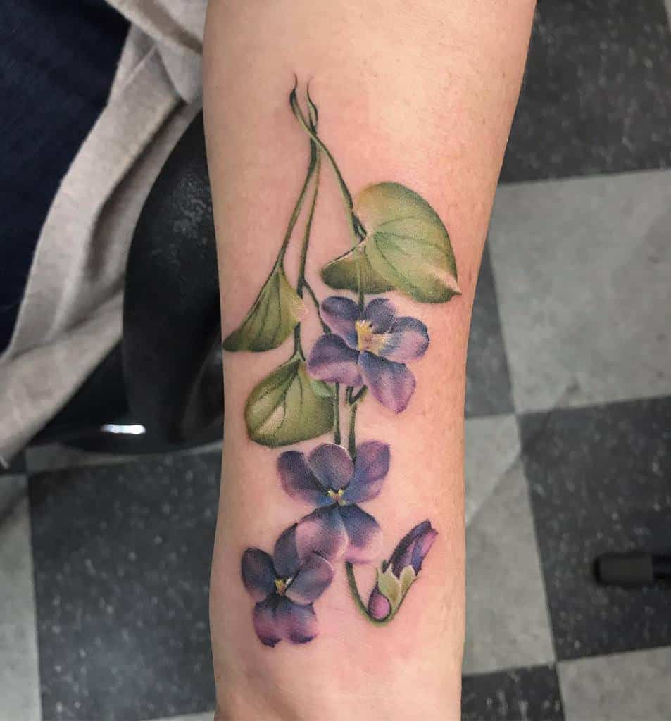 Delicate tattoo of violet flowers with lush green leaves, designed in a realistic style, symbolizing beauty, love, and tranquility