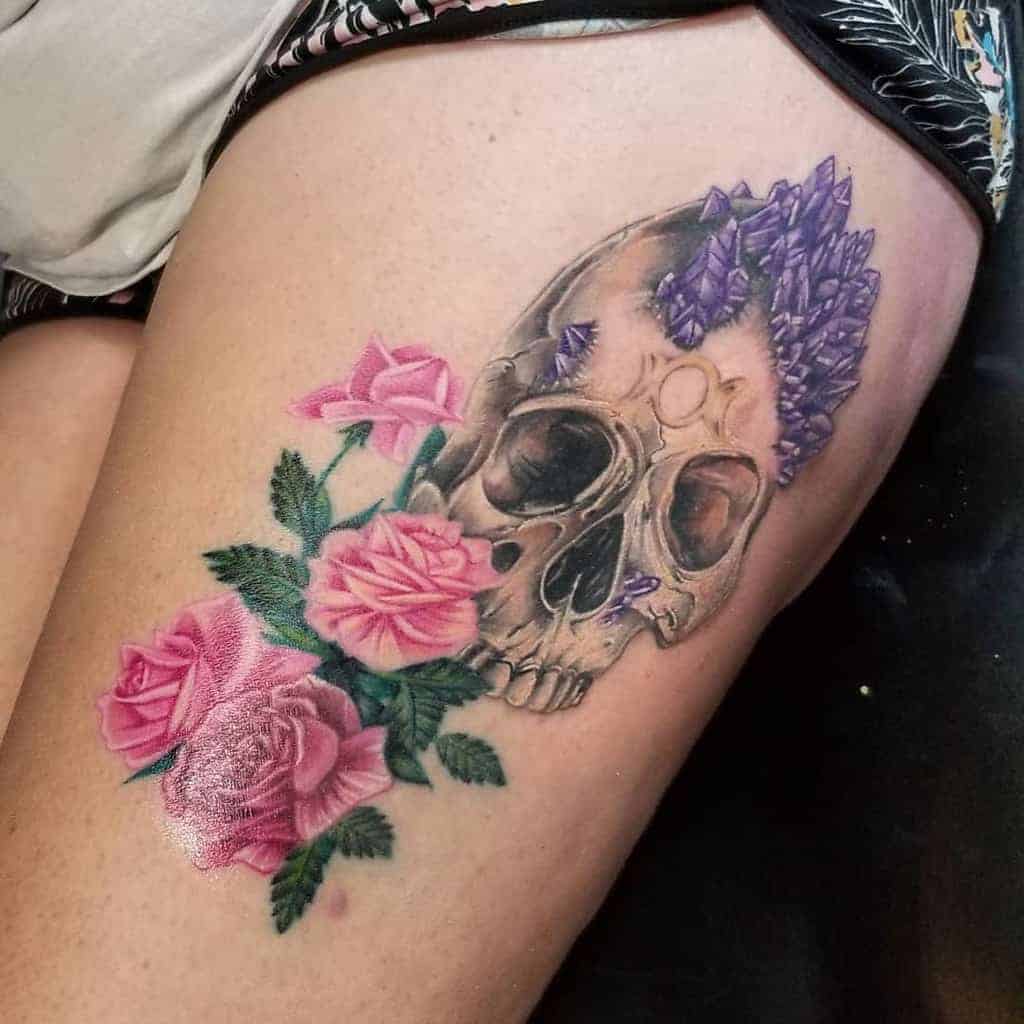 Tattoo of a crystal-covered skull with pink roses on a person's thigh