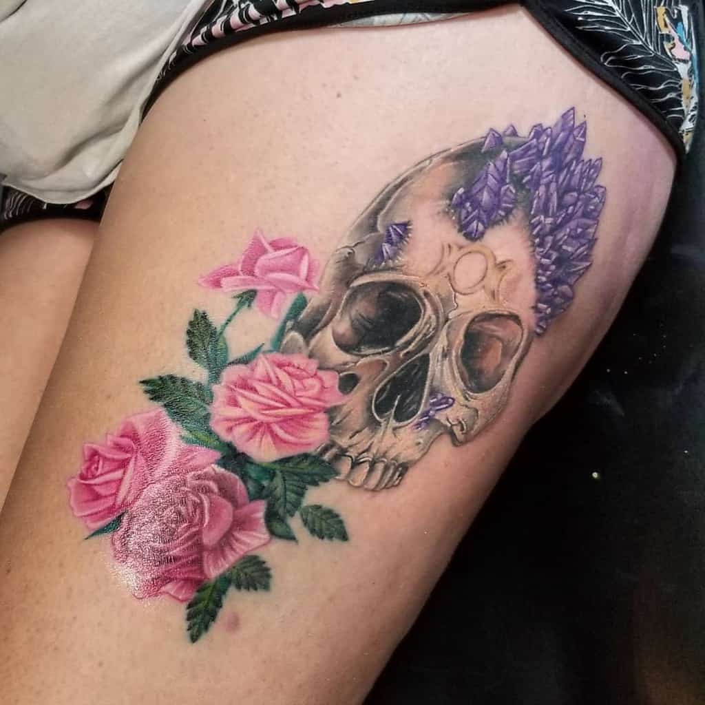 Thigh tattoo of a skull with purple crystals and pink roses, blending realism with mystical and floral elements in a vibrant design.