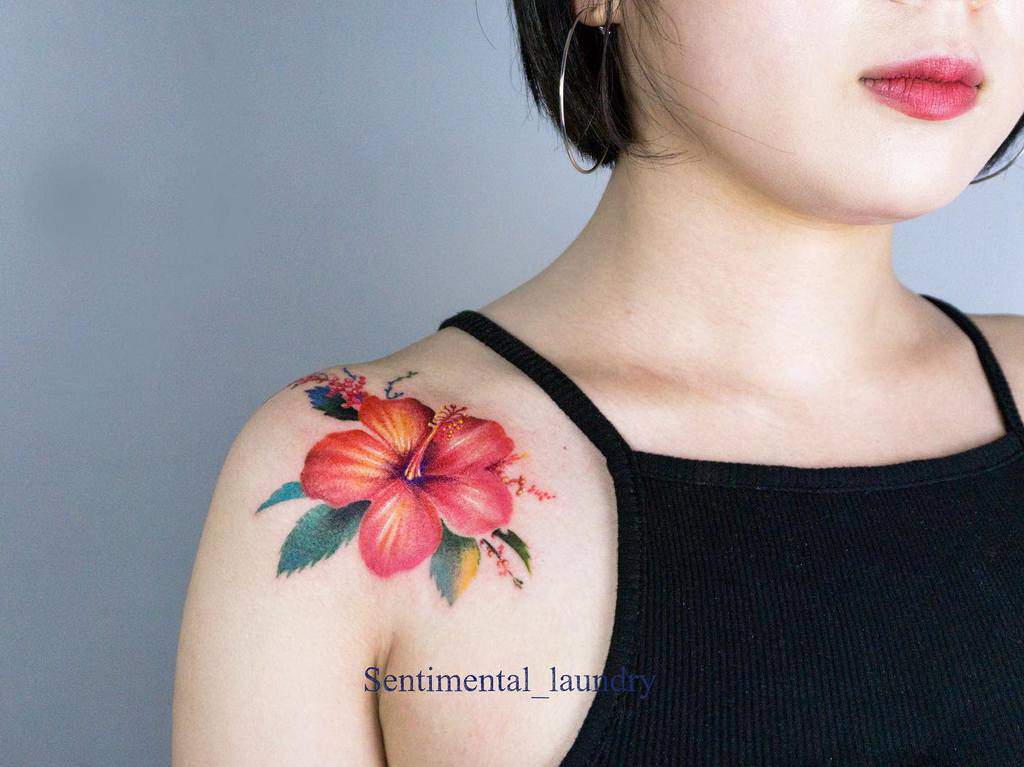 A woman adorned with a red hibiscus tattoo gracefully inked on her shoulder