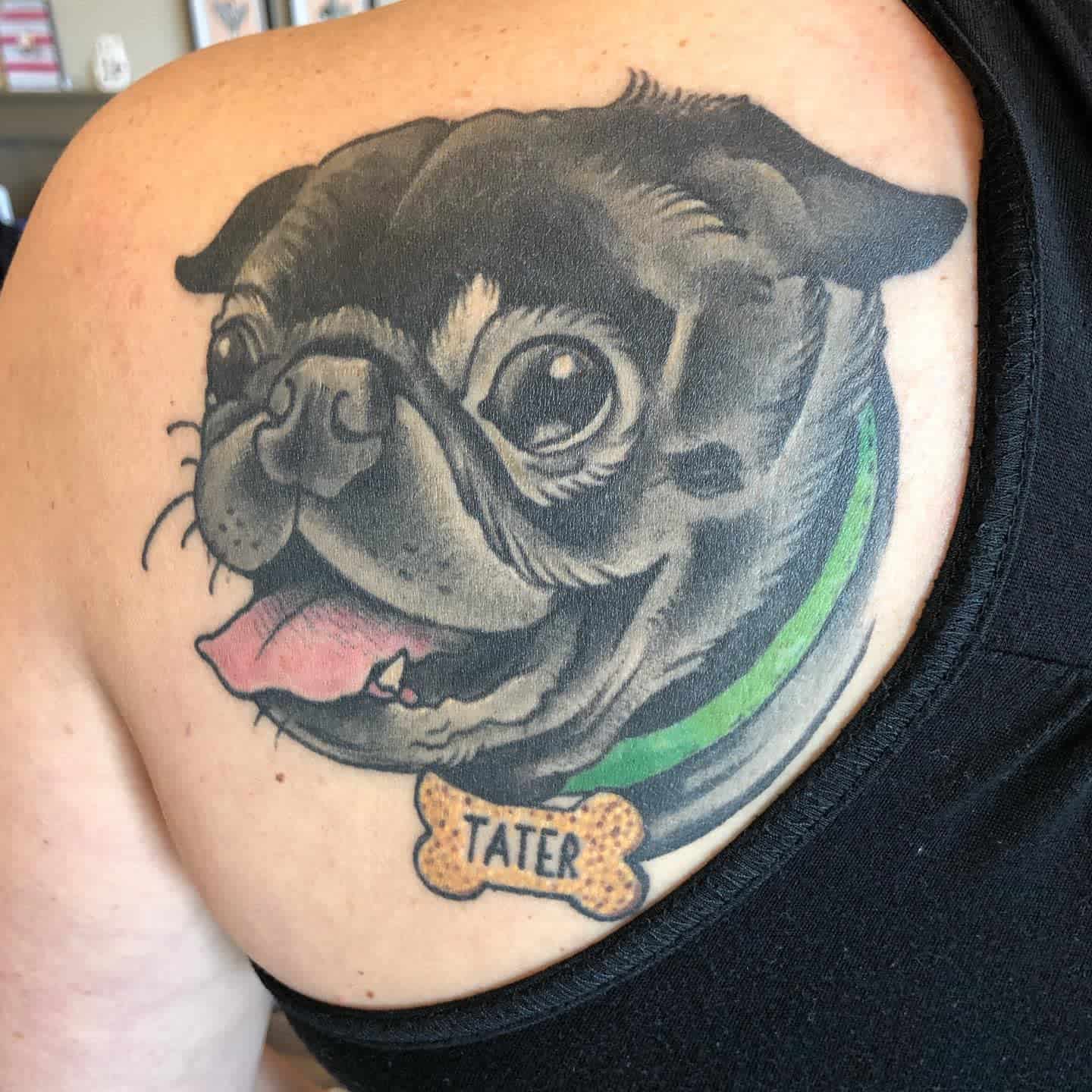 A colorful tattoo of a smiling pug with a green collar and "Tater" written on a bone-shaped tag 