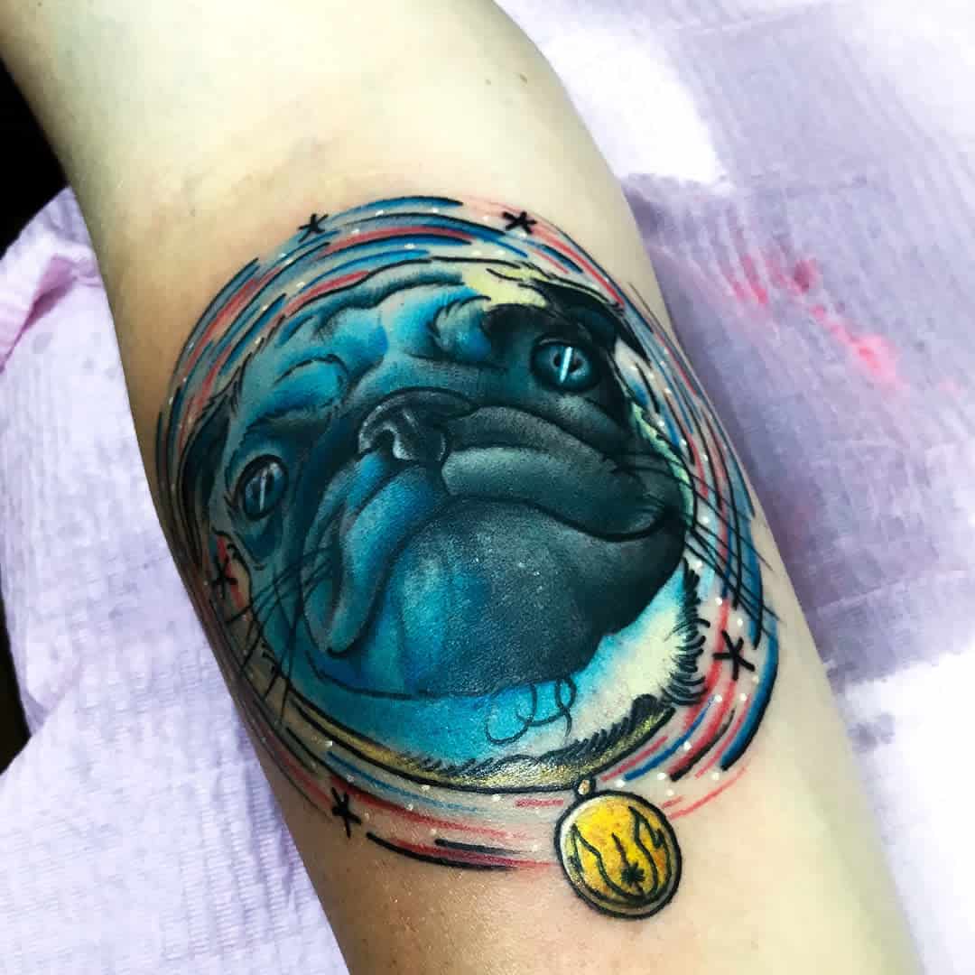 Tattoo of a pug with a blue hue and a gold pendant, surrounded by a circular, colorful design