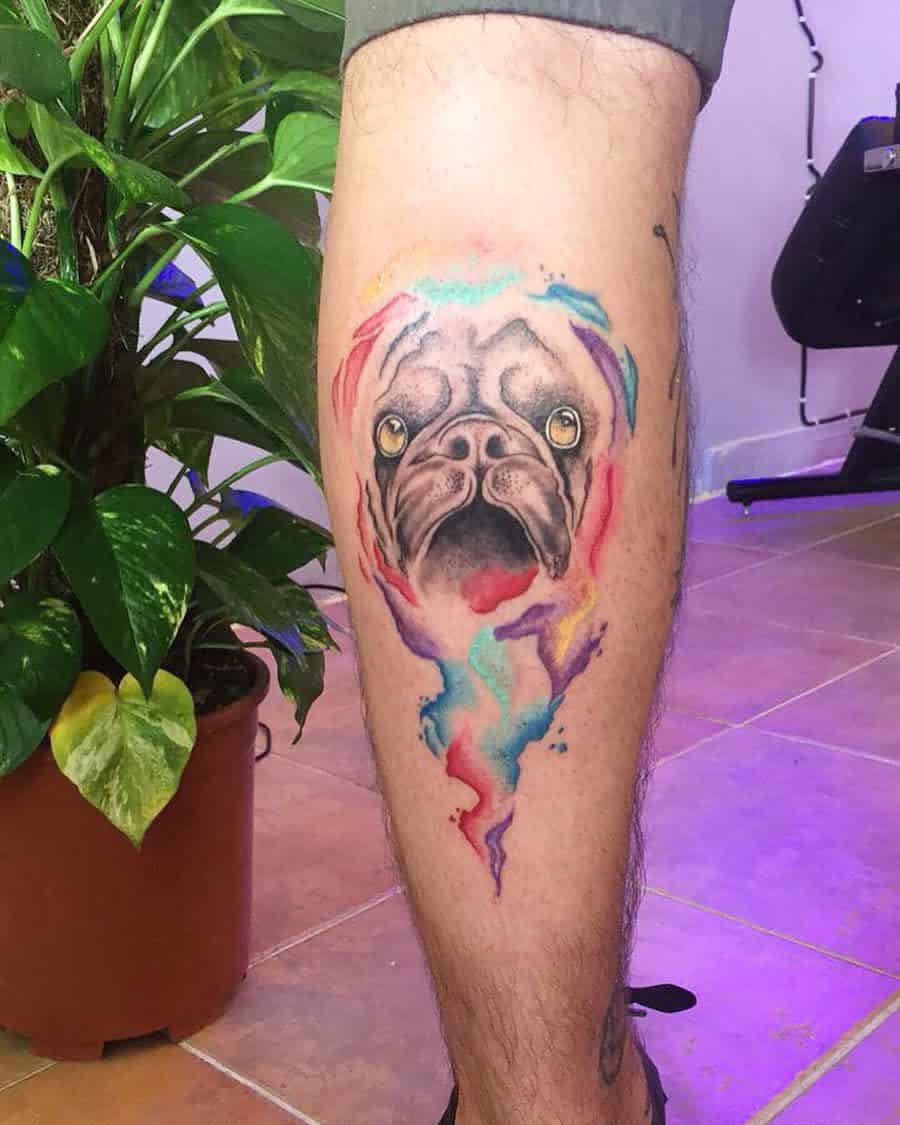 A colorful tattoo of a pug's face surrounded by vibrant splashes of watercolor paint