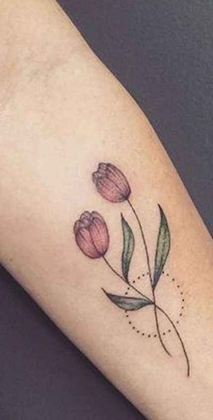 A colorful tulip tattoo on the forearm featuring two flowers with soft purple petals, delicate leaves, and a dotted circle accent.