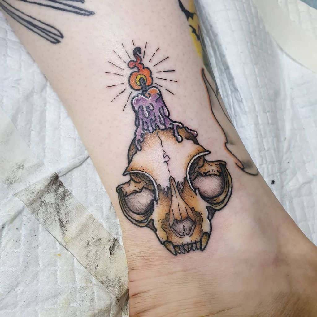 Tattoo of a candle melting over a cat skull on an ankle