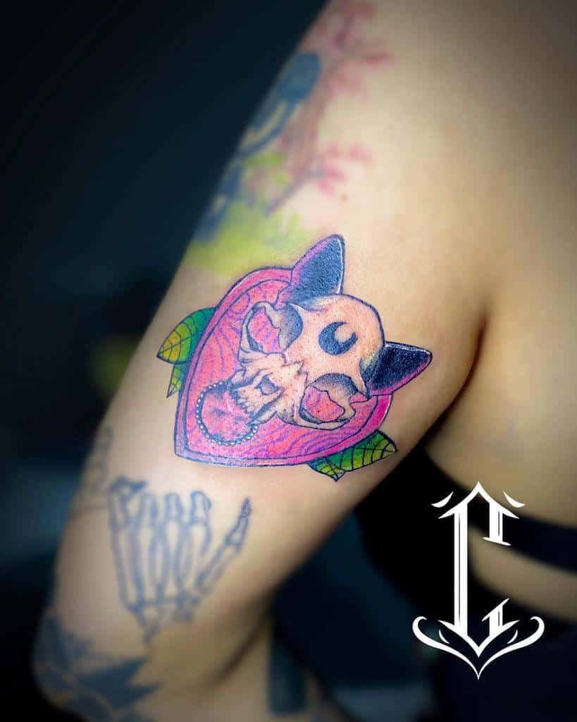 Tattoo of a cat skull intricately surrounded by a heart and delicate leaves on an upper arm
