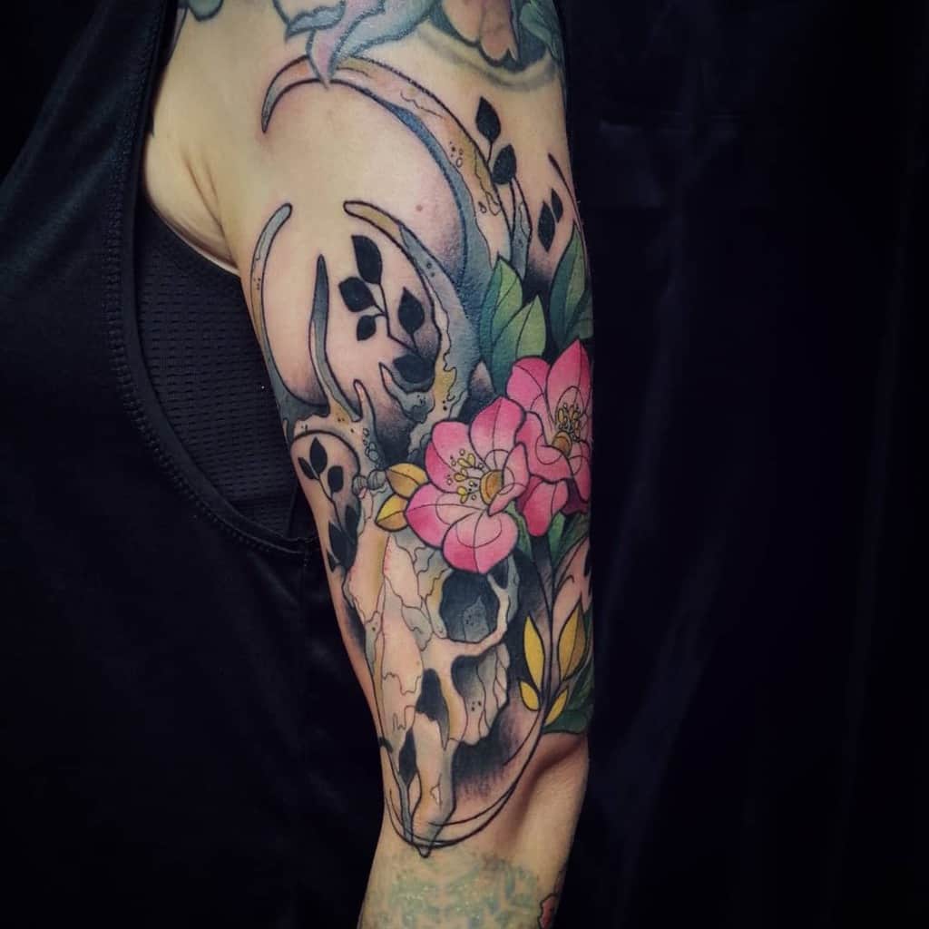 Colorful tattoo of a deer skull and flowers on a person's upper arm