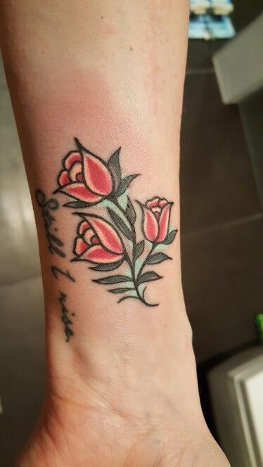 A bold traditional-style tulip tattoo on the wrist, featuring three red flowers with green leaves and the phrase "Still I rise" in cursive.