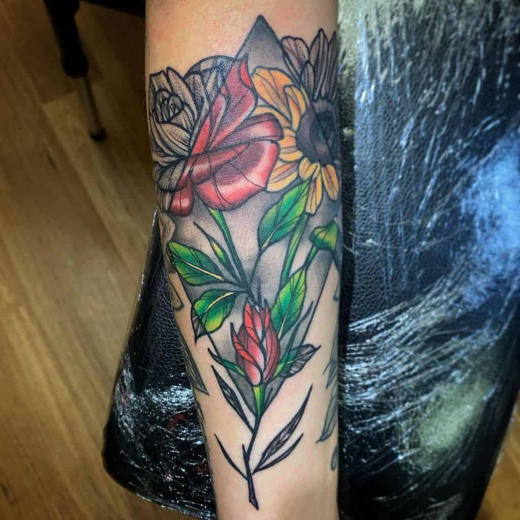 Vibrant geometric flower tattoo featuring red, yellow, and green tones with intricate leaf details on the forearm