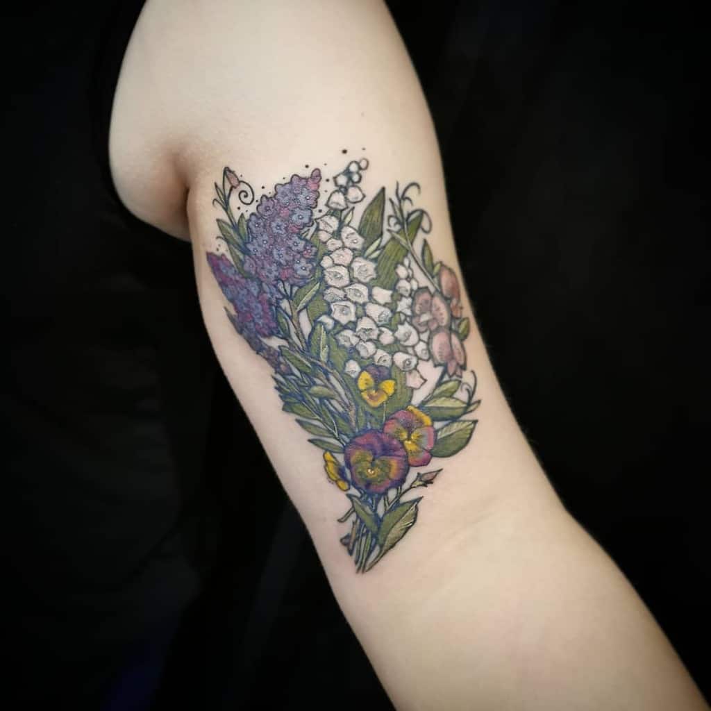 Colorful floral bouquet tattoo, featuring Lily of the Valley, lilacs, violets, and greenery in a delicate botanical style