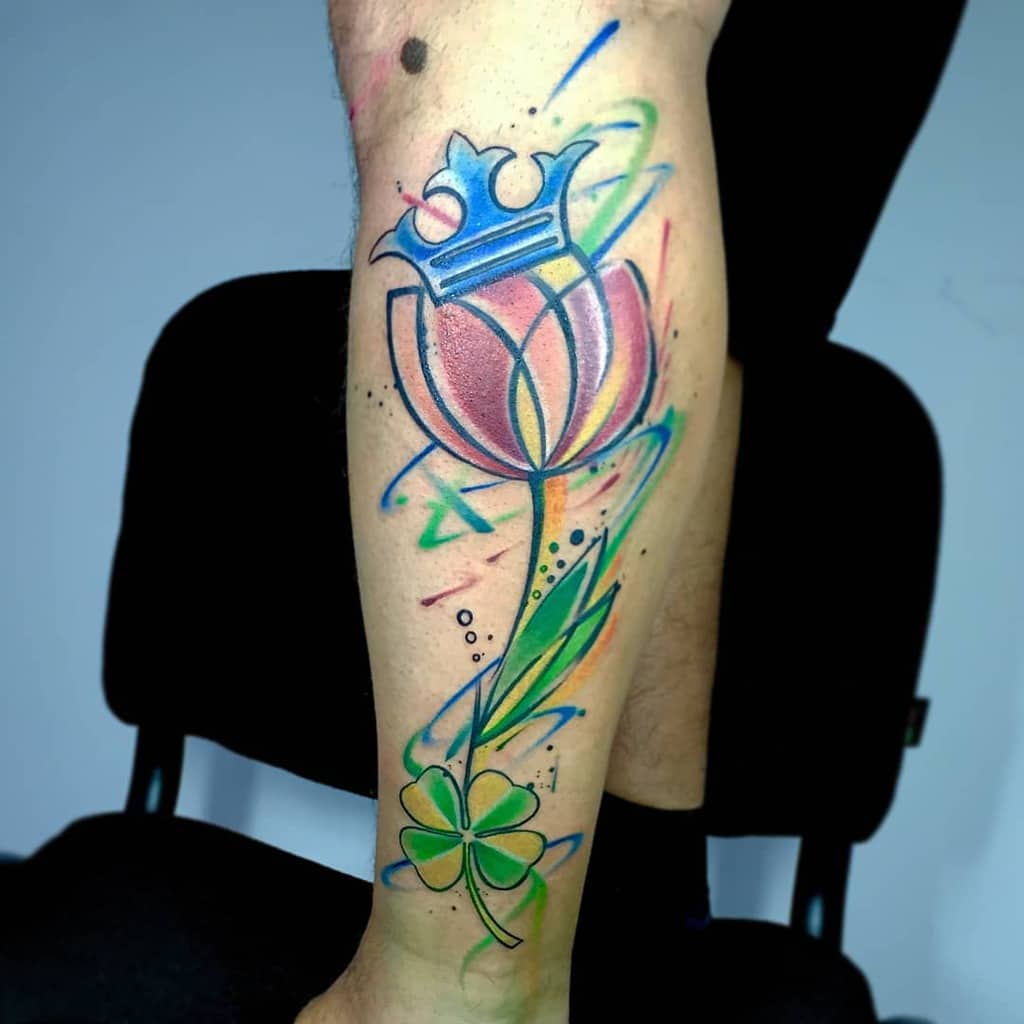 Watercolor-style tattoo of a tulip with a crown and a clover on a person's leg, featuring vibrant colors
