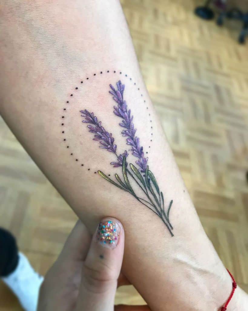 A lavender tattoo with a circular dotted design, featuring two purple lavender stems surrounded by delicate greenery.