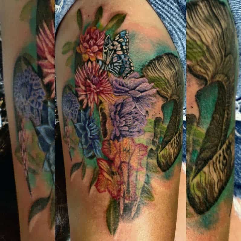 Colorful floral tattoo with butterflies, a ram skull, and mushrooms on an upper thighh