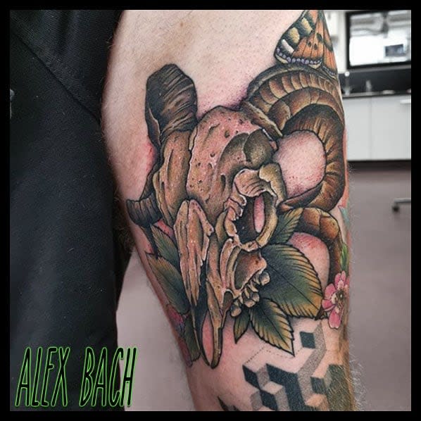 Tattoo of a ram skull adorned with flowers and a butterfly on an upper arm