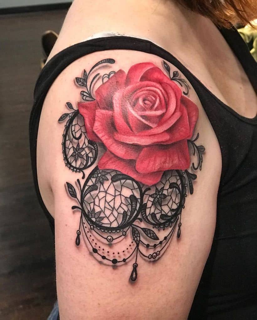 Upper arm tattoo featuring a realistic red rose with intricate black lace details, ornamental filigree, and delicate beaded chains.