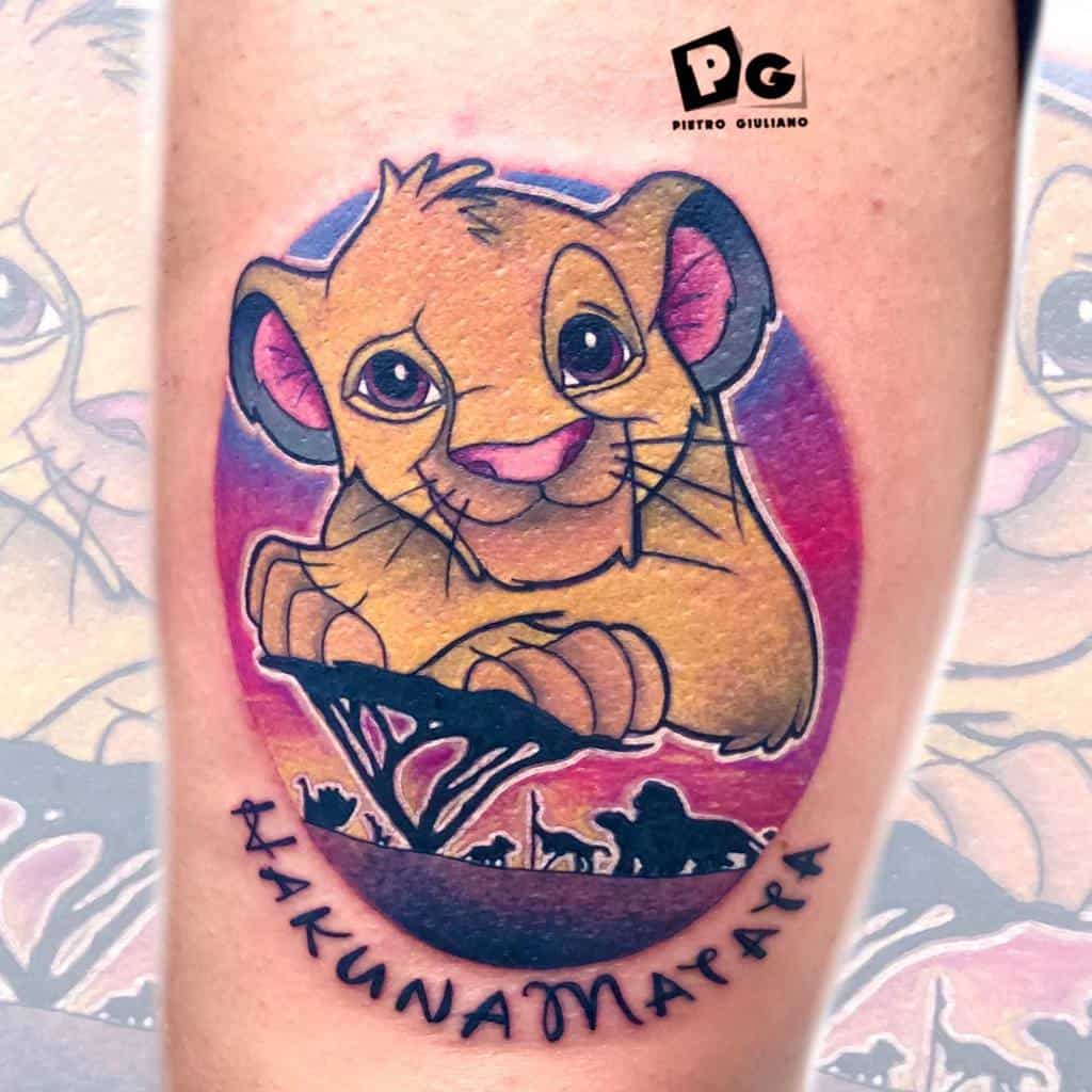 Colorful tattoo of Simba as a cub with a vibrant sunset background, a silhouette of animals beneath, and the phrase 'Hakuna Matata' below