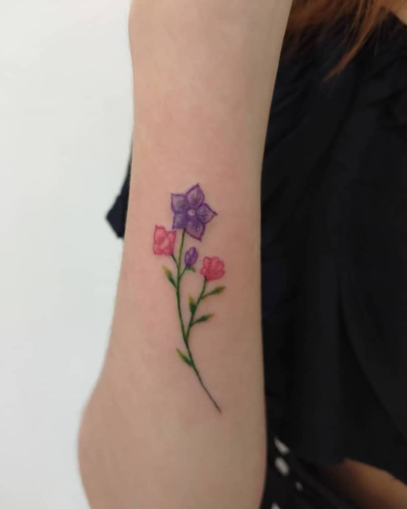 Forearm tattoo of purple and pink flowers with green stems and leaves