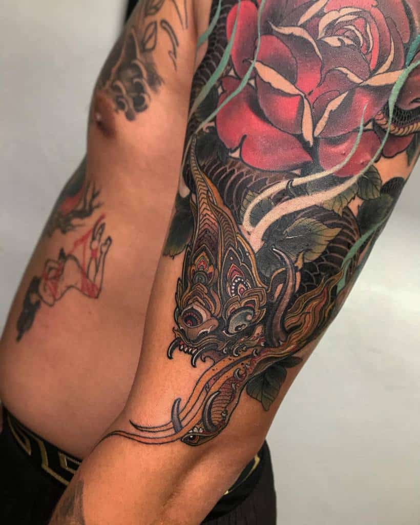 Tattooed arm with colorful dragon and rose designs on a person's upper body
