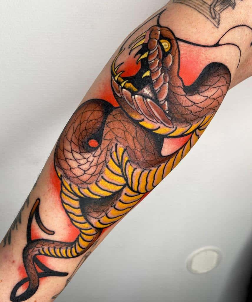 Tattoo of a coiled snake with an open mouth on a person's arm, featuring detailed shading and a vibrant color palette