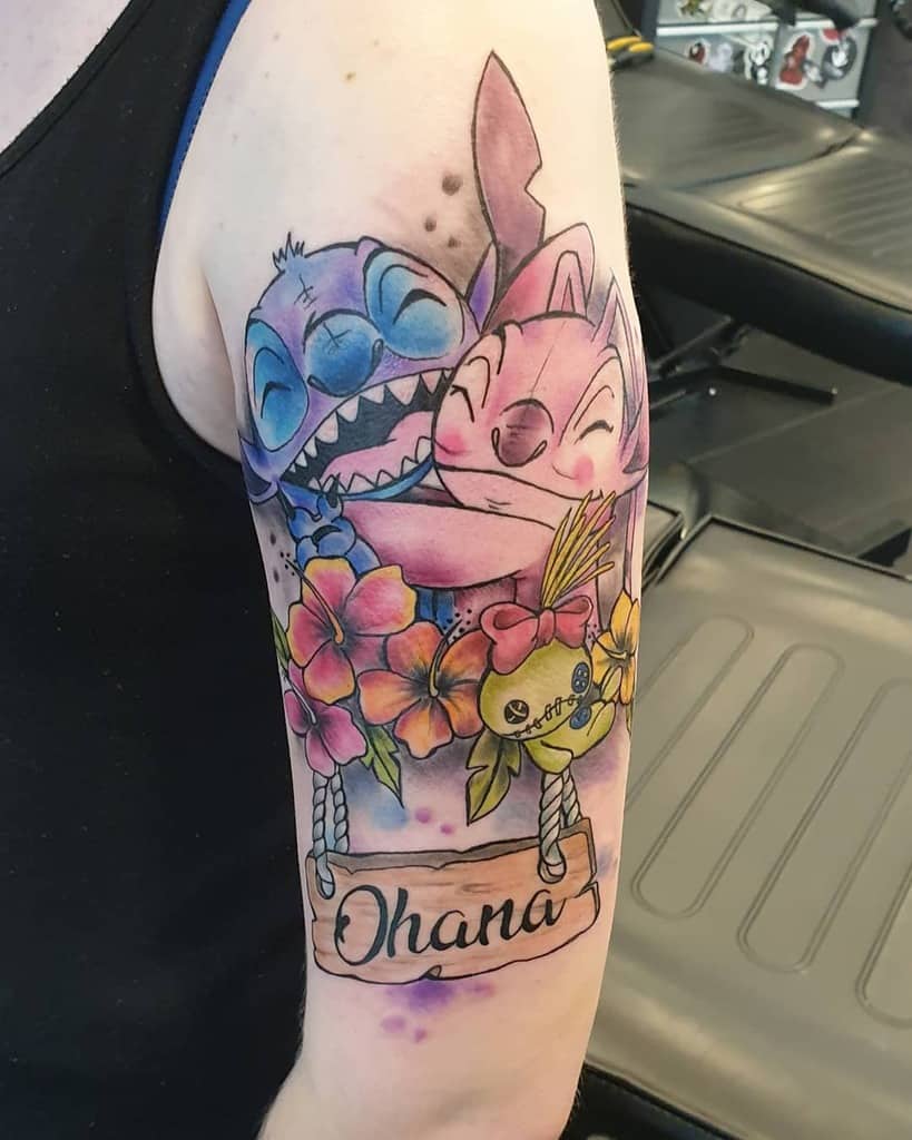 Colorful tattoo of Stitch and Angel hugging with hibiscus flowers and an 'Ohana' sign, symbolizing love, family, and Hawaiian culture.