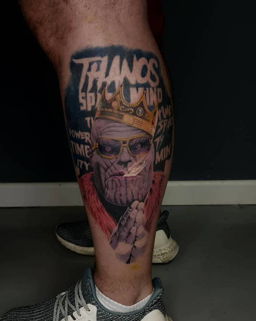 A tattoo of Thanos wearing a crown and sunglasses, with the word "THANOS" in bold text above and various phrases like "SPACE," "TIME," and "POWER" surrounding him