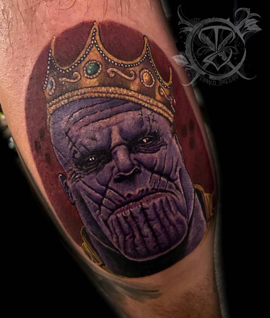 A vibrant tattoo of Thanos wearing a golden crown, with his intense expression and detailed purple skin in red circle background