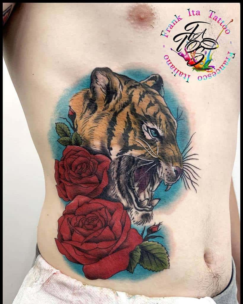 A majestic tiger is intricately tattooed alongside vibrant red roses on a person's side, creating a striking and powerful display of art